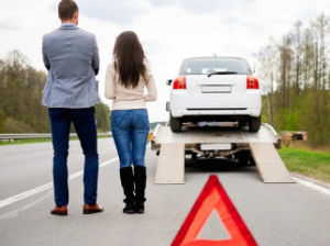 man and woman couple standing on the side of the road as their car gets put on a tow truck