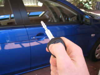 hand holding up a key in front of a blue car