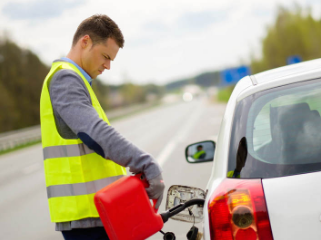tow truck worker wearing a bright yellow vest delivering fuel to a car on the side of the road